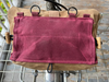 A tan canvas utility pouch with a large dusty rose pink rectangular fabric panel attached to the front, hanging from a metal grid rack.