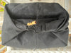 A black canvas dry bag or pouch with a rolled top closure, secured by a black strap and metal ring, featuring a small orange-brown wooden toggle, photographed outdoors on a porch.