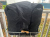 A black fabric bag with a wooden toggle clasp resting on a metal wire bicycle basket, set against an outdoor residential background.