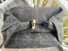 A dark gray waxed canvas bag with a rolled top closure, secured by a black strap and toggle clasp with a light wood accent, photographed outdoors on a wooden deck.