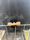 Close-up of a dark gray canvas bag secured with a black strap and a light natural wood toggle on a metal rack.