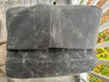 A folded dark gray fabric item, likely a blanket or throw, with a distressed waxed-paper texture, resting on a white porch chair outdoors.