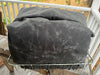 A dark gray waxed canvas cover, likely for a grill or smoker, draped over a metal wire rack on a wooden deck with a white railing and outdoor foliage in the background.