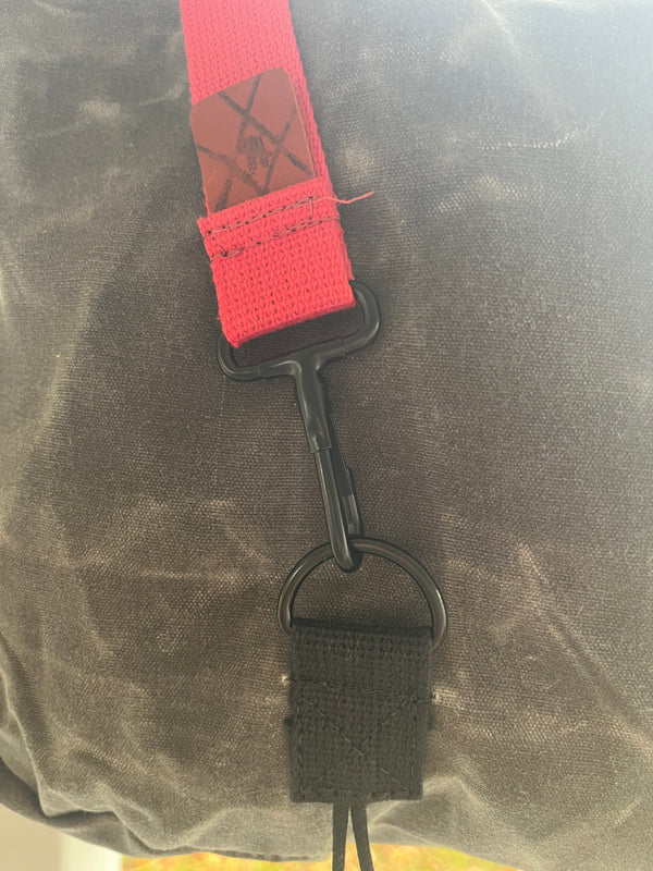 Close-up of a dark gray fabric bag with a bright red webbing strap, black metal carabiner, and black webbed loop attachment.